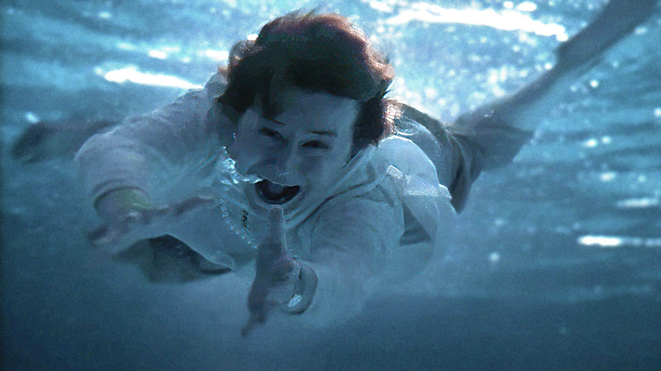 A terrified woman swims underwater toward the camera.
